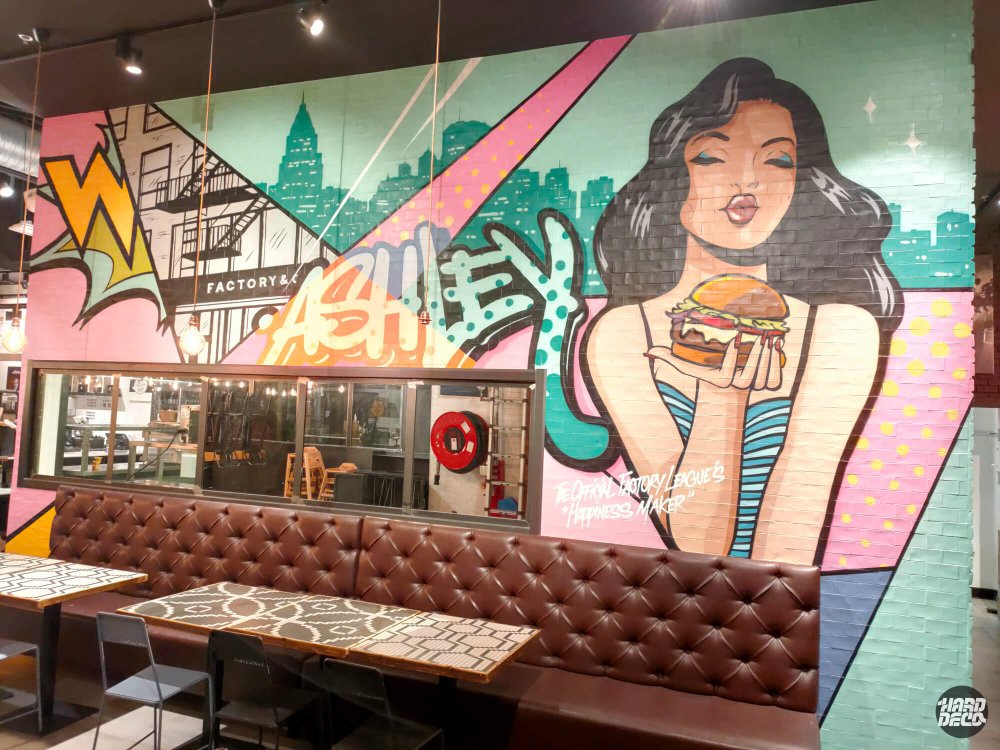 Détail fresque pop art Ashley mascotte Factory & Co tenant un burger, skyline Manhattan fond vert