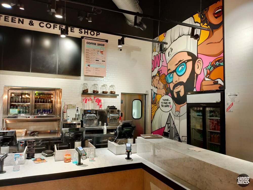 Vue du comptoir coffee shop Factory & Co avec fresque pop art chef et personnages colorés en fond