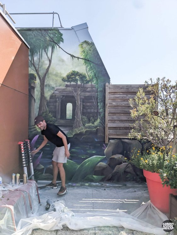 Artiste Chek posant devant la fresque temple jungle en cours de réalisation sur terrasse