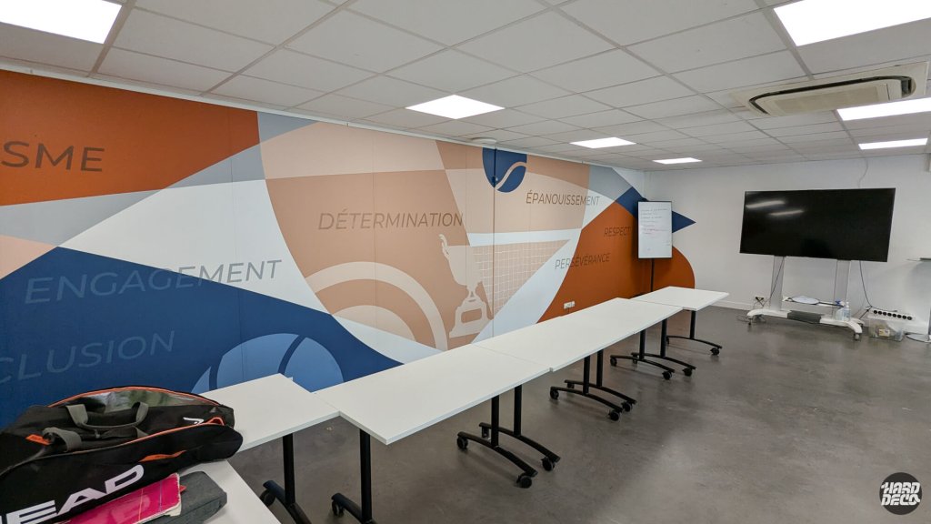 Salle de réunion avec fresque murale typographique bleu orange saumon, valeurs du club de tennis