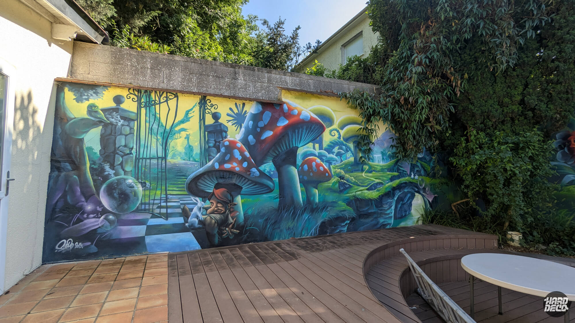 Fresque murale aérosol sur terrasse : forêt féerique avec champignons géants rouges, gnome et portail fer forgé
