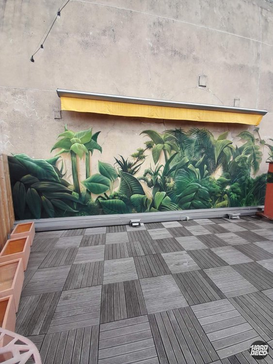 Détail fresque jungle extérieure à l'aérosol, feuillage tropical dense sur enduit béton craquelé