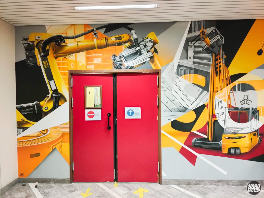 Gros plan fresque Sodis bras robotisé KUKA jaune et chariot élévateur encadrant les portes rouges du hall