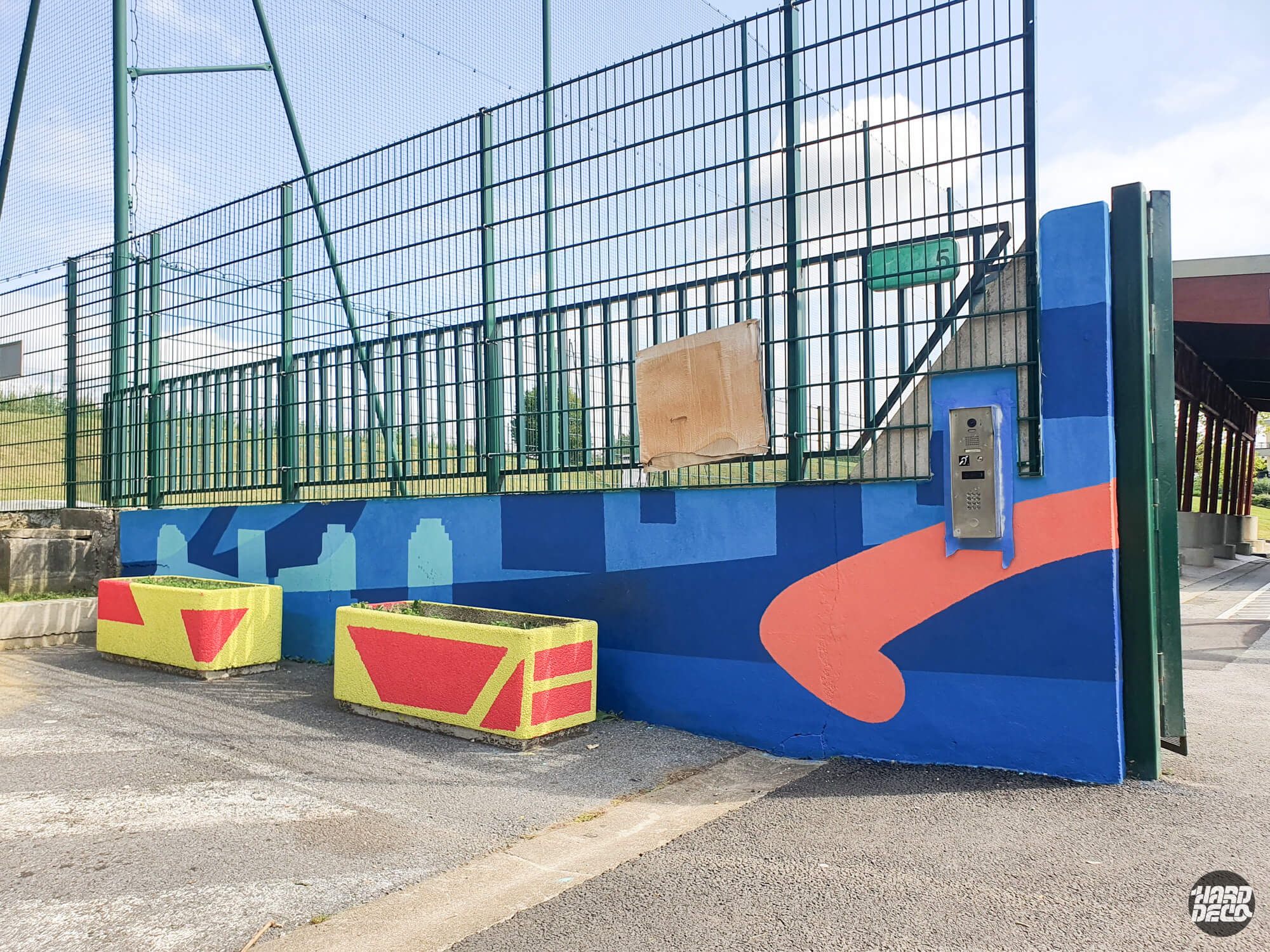 Fresque murale géométrique bleue et orange sur muret d'école à Torcy, bacs à fleurs peints en jaune et rouge