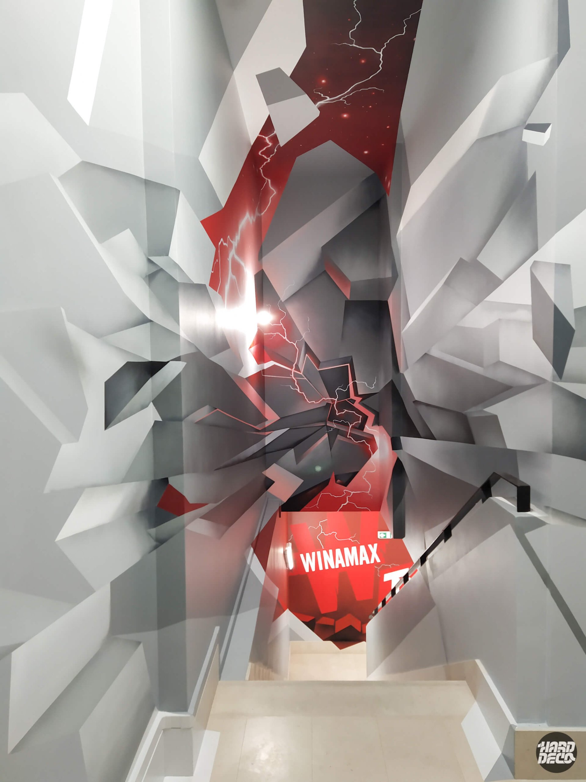 Vue plongeante cage d'escalier Winamax TV Paris, fresque 3D géométrique gris blanc et rouge avec éclairs