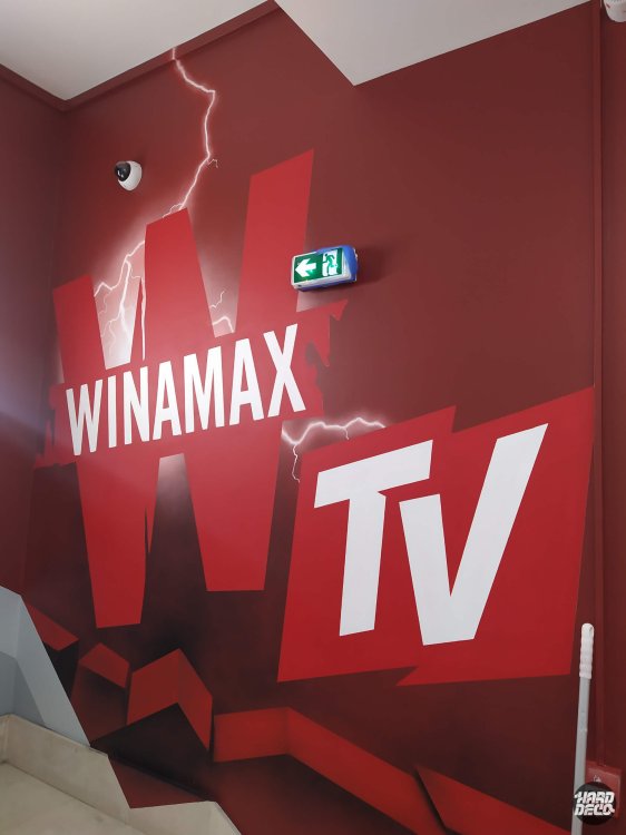 Détail logo Winamax TV peint sur fond rouge carmin, lettrage blanc et éclairs, angle palier escalier