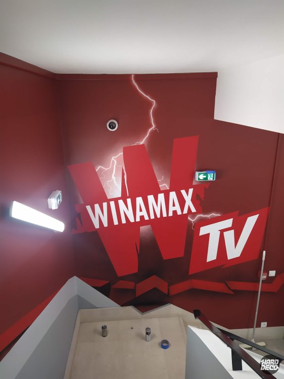 Mur rouge Winamax TV avec logo monumental et éclairs peints, décoration murale bureaux Paris