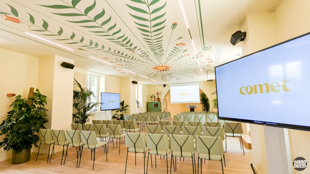 Salle de conférence Comet Meetings avec fresque végétale au plafond, chaises céladon et écrans