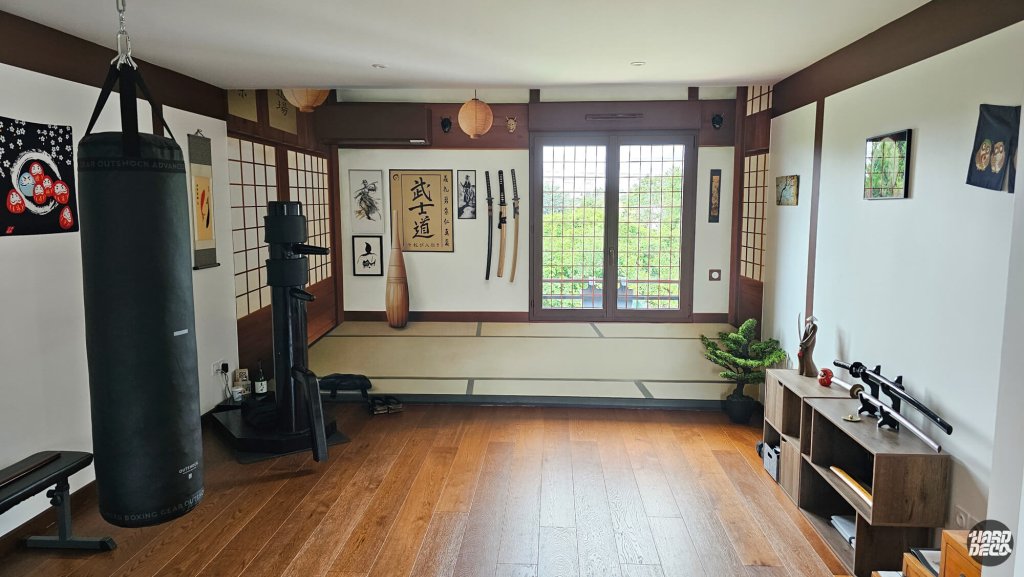 Salle de sport transformée en dojo japonais par trompe-l'œil : poutres brun-acajou, tatamis et katanas suspendus
