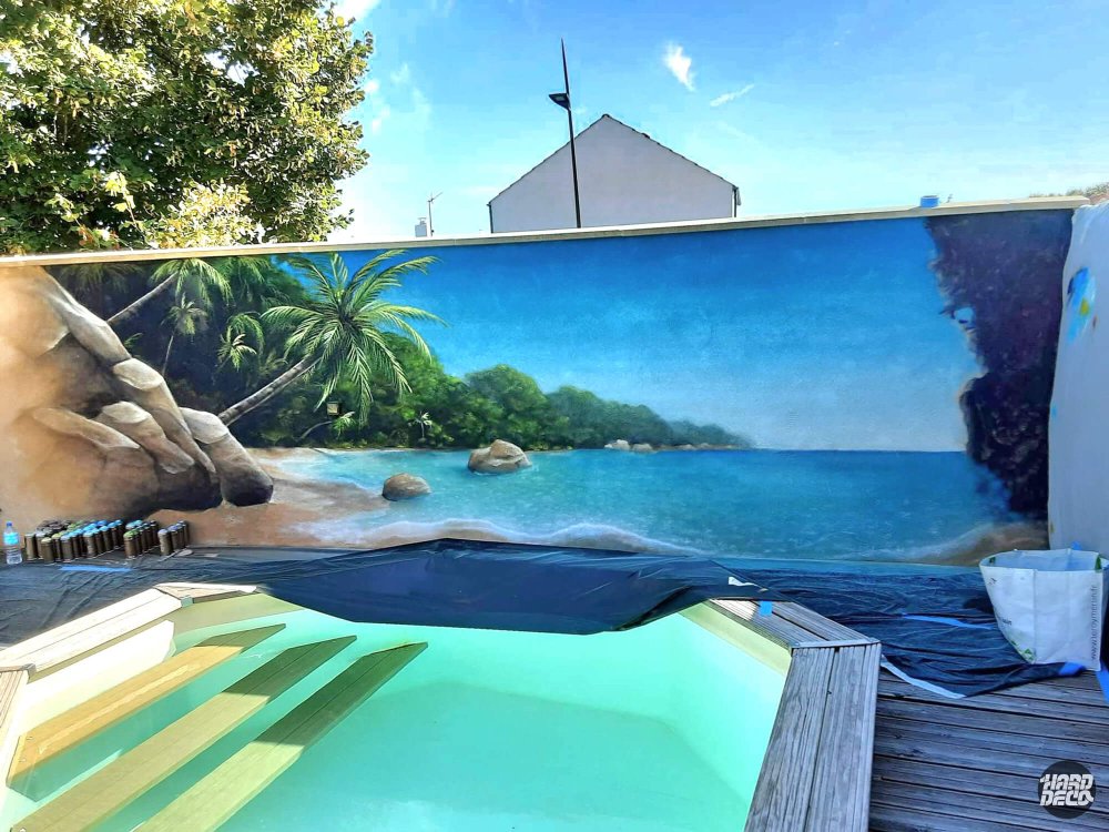 Fresque trompe-l'œil plage tropicale à l'aérosol sur mur de clôture en cours de réalisation, bord de piscine
