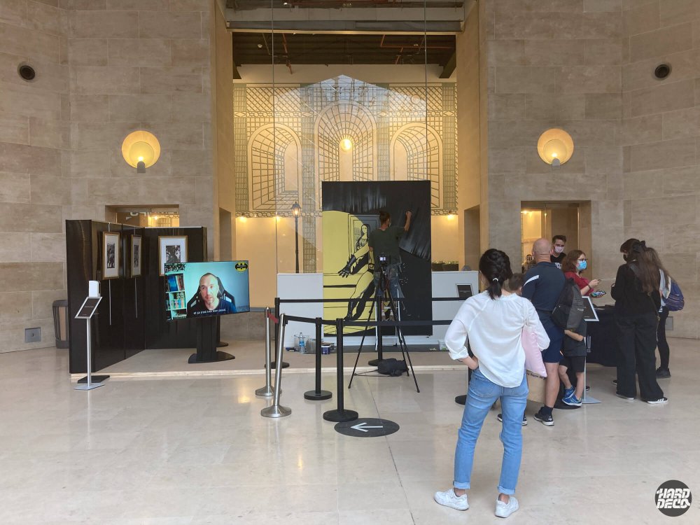 Vue d'ensemble du hall du Louvre avec toile Batman en cours de peinture et public de visiteurs, Batman The World