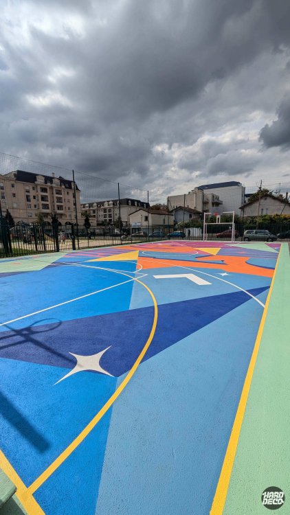 Sol sportif peint en bleu cobalt et orange, terrain de basket Livry-Gargan, motifs géométriques et étoiles