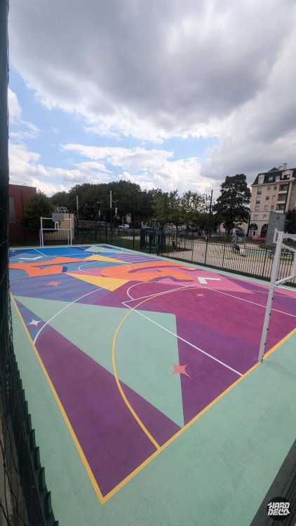Terrain de basket Livry-Gargan vu de côté, motifs géométriques violet, rose, vert et orange sur sol sportif