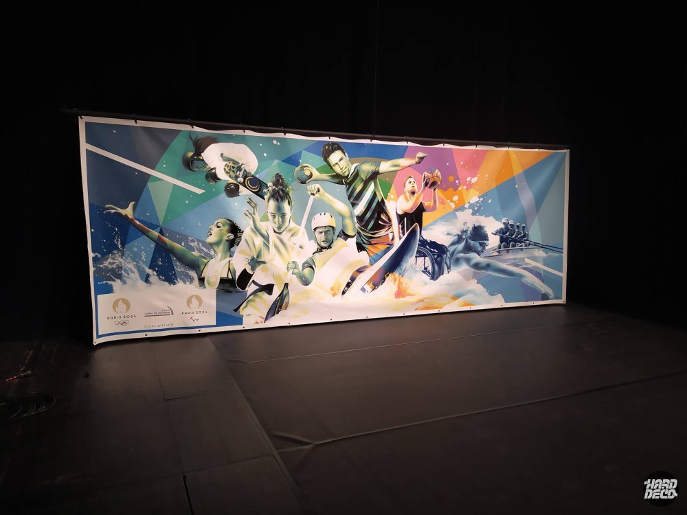 Toile aérosol Paris 2024 posée au sol, vue d'ensemble avec athlètes olympiques et paralympiques, fond géométrique coloré
