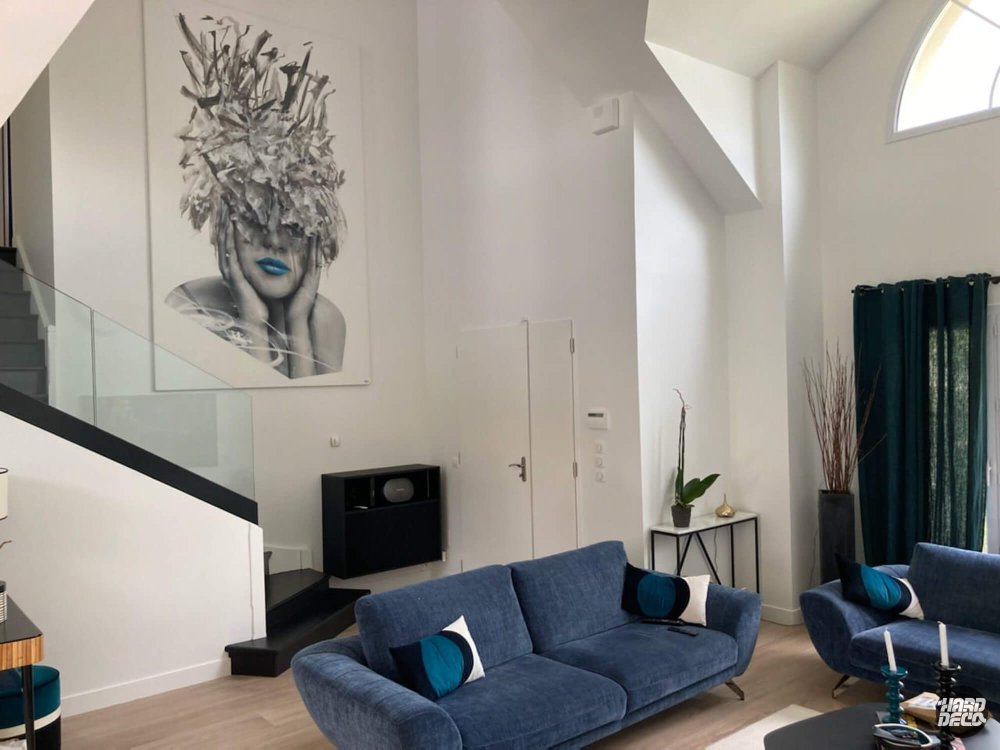 Vue ensemble salon double hauteur avec toile portrait féminin gris blanc bleu sur mur blanc épuré