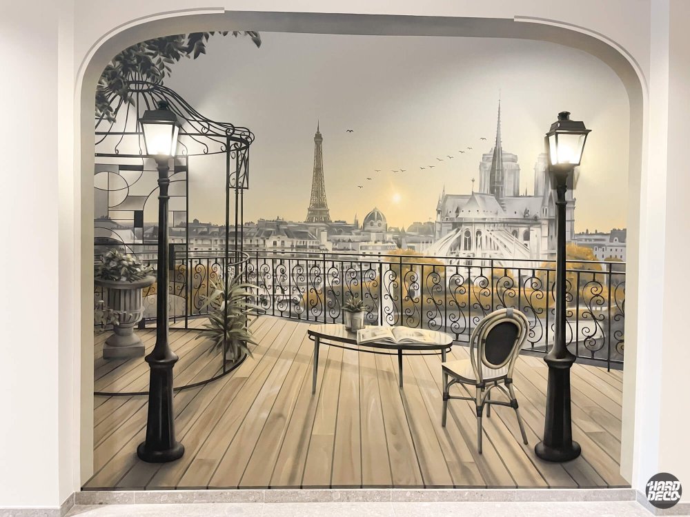Trompe-l'œil terrasse parisienne peinte dans un hall d'entreprise, Tour Eiffel et Notre-Dame au fond, lampadaires intégrés