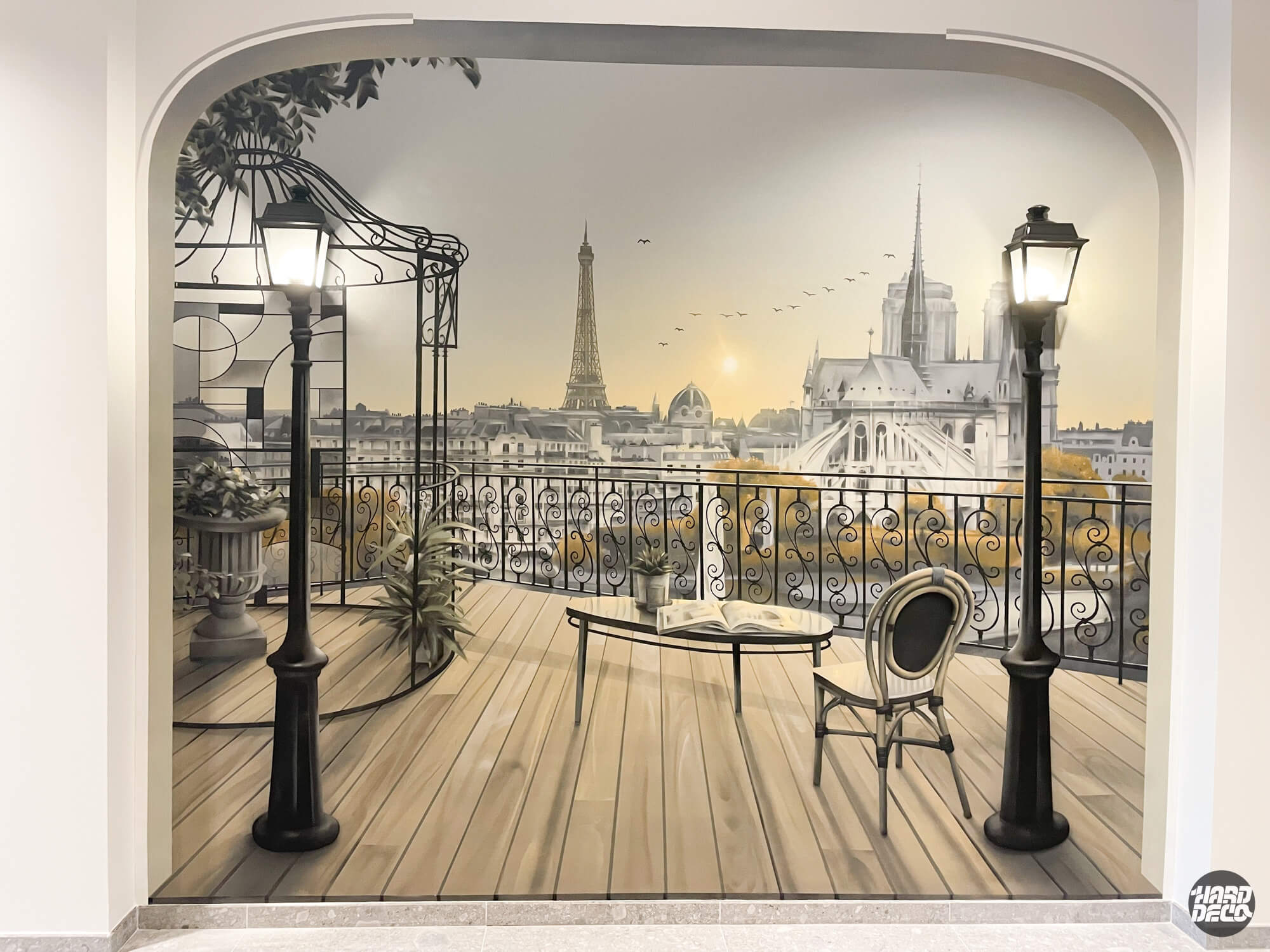 Trompe-l'œil terrasse parisienne peinte dans un hall d'entreprise, Tour Eiffel et Notre-Dame au fond, lampadaires intégrés