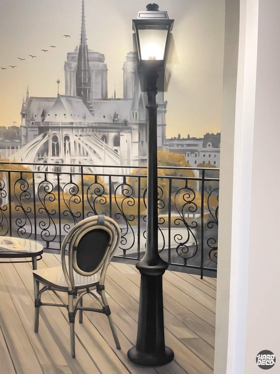 Détail lampadaire parisien réel intégré au trompe-l'œil mural, chaise bistrot et Notre-Dame peints en arrière-plan