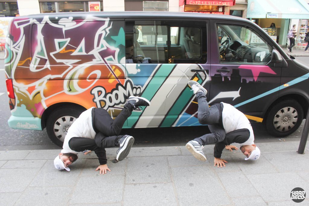 Van UE Boom graffiti hip-hop avec lettrage wildstyle orange et turquoise, deux danseurs en headstand devant