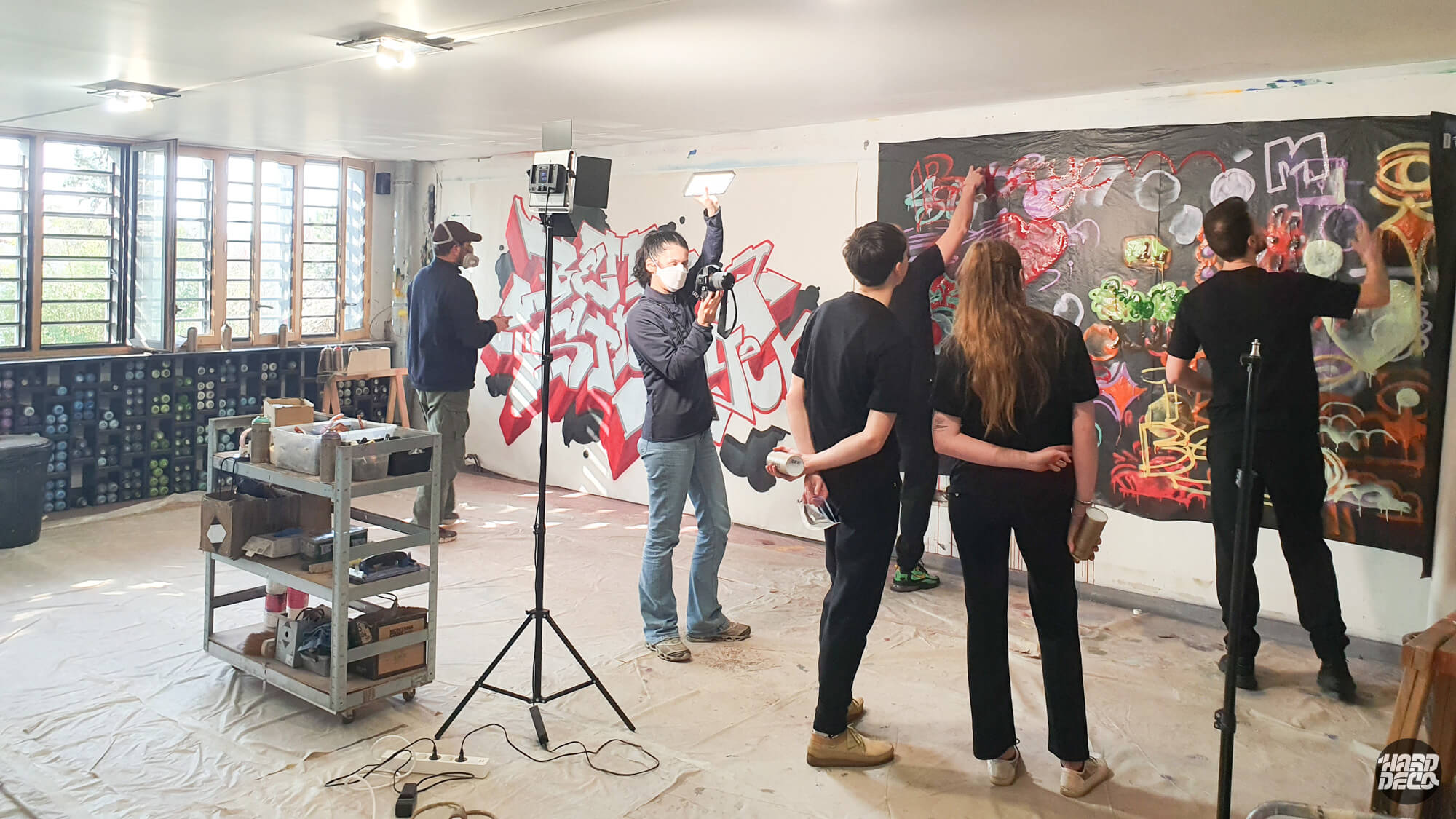 atelier intérieur avec plusieurs artistes en action créant un graffiti mural coloré sur un mur blanc