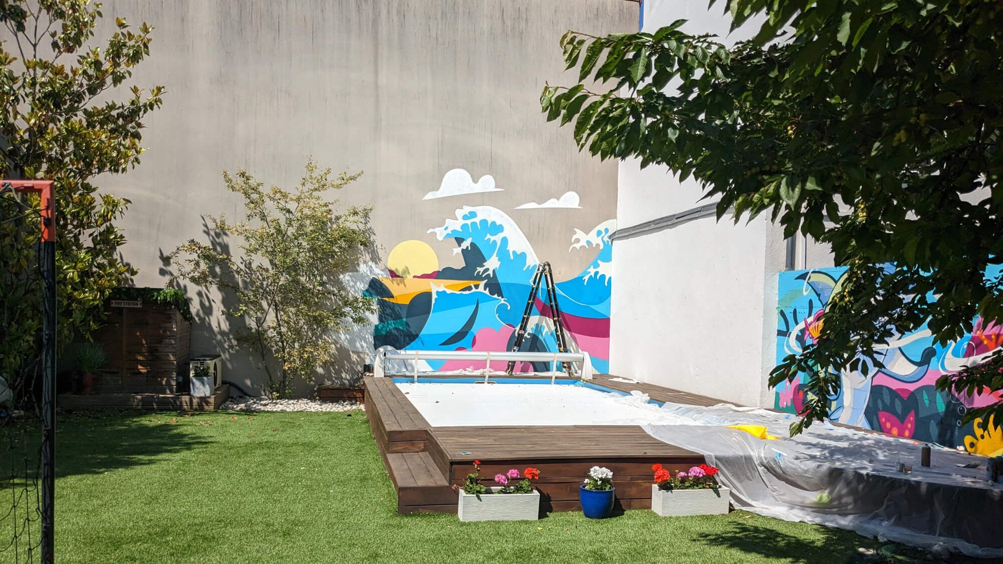 Vue d'ensemble du jardin avec piscine et fresque vague Hokusai en cours de réalisation sur mur en béton