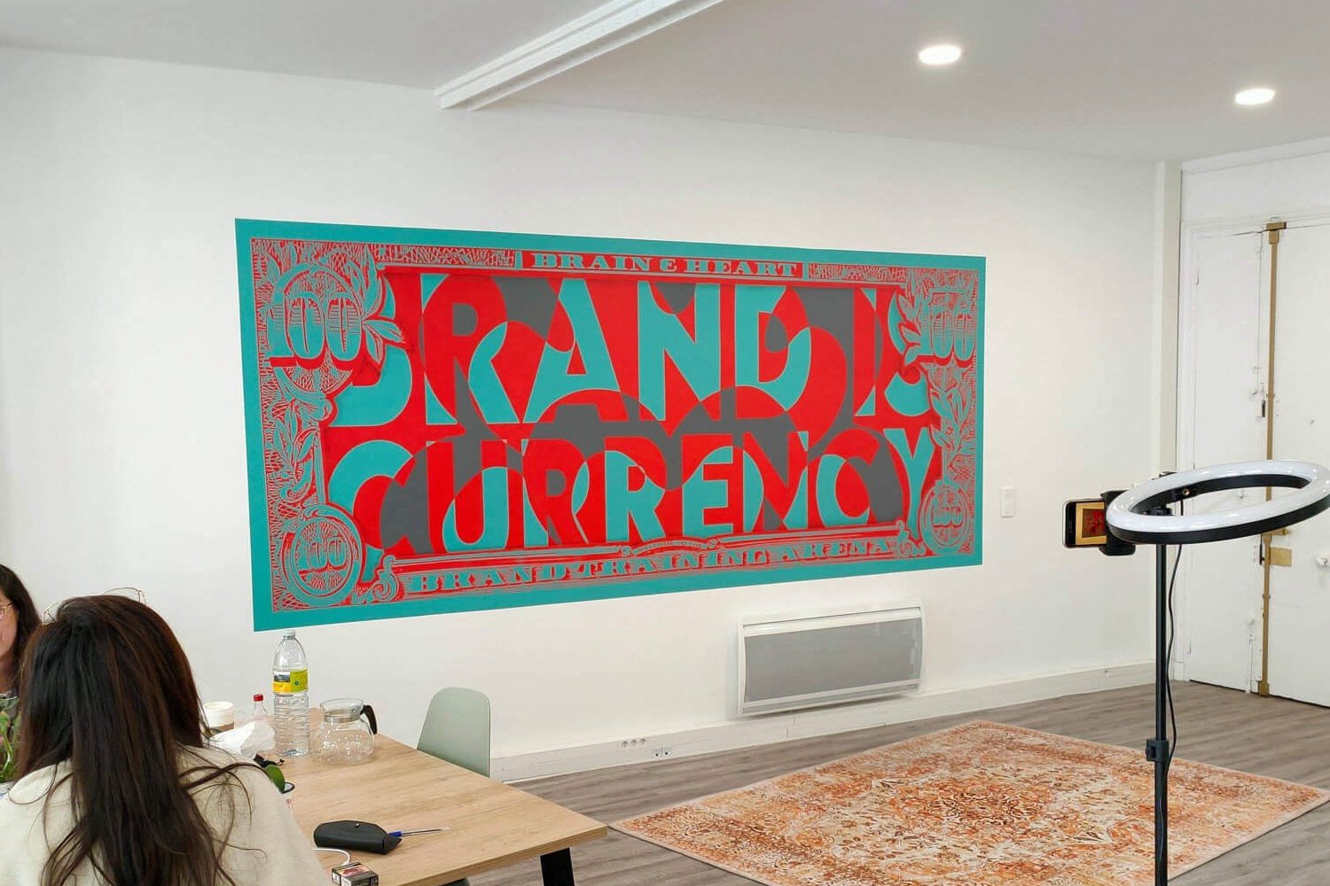 Open space agence Brain & Heart Paris avec toile murale billet dollar détourné rouge turquoise